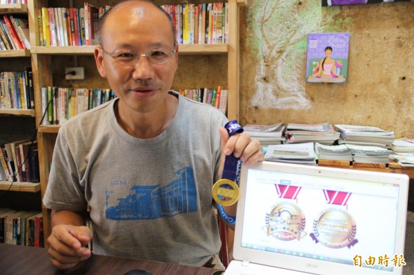 新竹縣關西鎮藝術小鎮發展協會總幹事盧文鈞展示今年的「關西小鎮路跑賽」東安古橋加上「採茶妹」造型的路跑玩賽獎牌圖案。(記者黃美珠攝)
