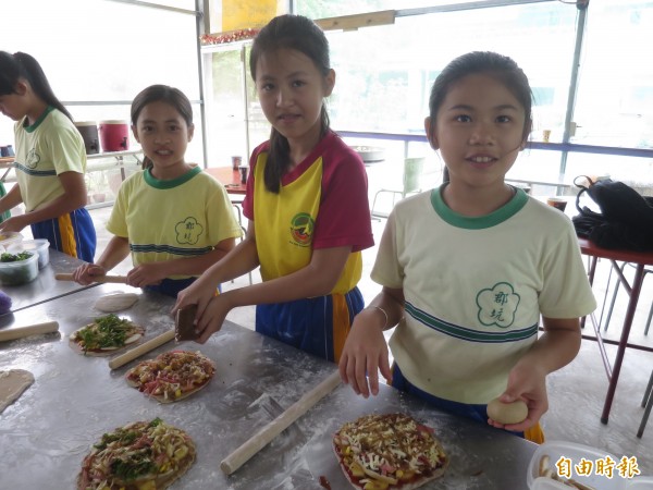 水里郡坑國小師生們跟著廚師將梅果、過貓野菜放進餅皮，親手製作特殊的梅子披薩。（記者劉濱銓攝）