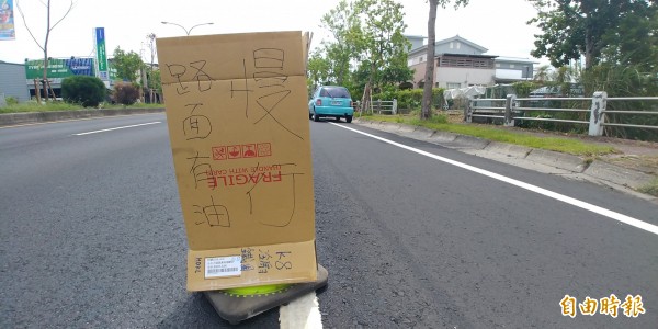 吊車漏油2公里，機車連環滑倒，駕駛舉牌提醒用路人小心。（記者簡惠茹攝）