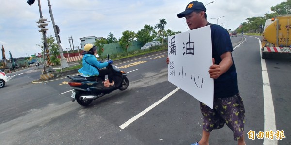 宋姓司機駕駛的起重機漏油，導致多輛機車慘摔，司機在路邊舉牌提醒騎士小心。監理所則提醒，機車騎上油漬別急按煞車，會出現水漂現象。（記者簡惠茹攝）