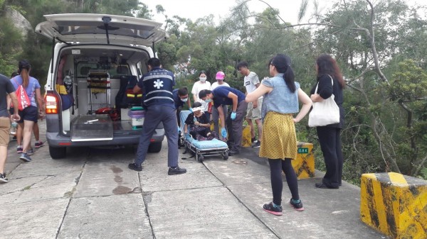 一名阿嬤疑遭登山人潮推擠跌落一旁駁坎,躺在擔架上由救護車救治。(圖由楊姓登山客提供)