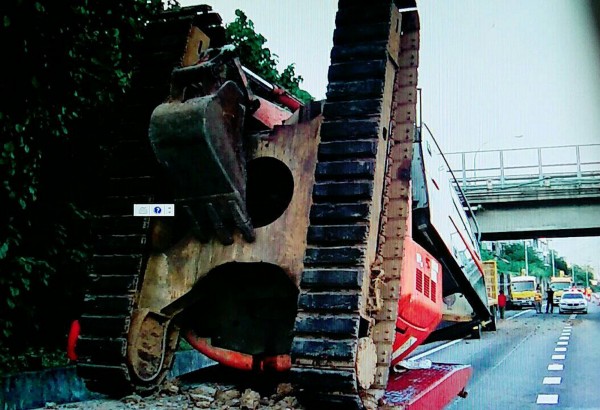 載運怪手的拖板車,疑因怪手挖臂未確實收妥,撞上國道陸橋後「倒頭哉」,導致板車後方升降板崩脫,液壓桿嵌刮到路面,拖板車無法行駛。(記者彭健禮翻攝)