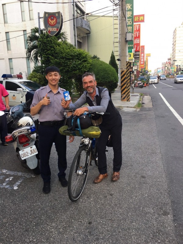 比利時男子騎單車環島，腳踏車「落鏈」，永康鹽行派出所員警充當黑手幫他修車，還請他喝飲料解渴。（記者黃文瑜翻攝）