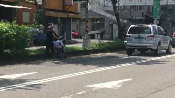 婦人推著坐有幼童的推車，走上快車道上，一路沿著路中央的樹蔭下行走。（記者劉濱銓翻攝）