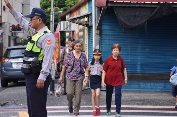 北埔國小四年級女童黃佳瑩化身「一日小女警」,為新城警分局擔任宣導大使執行「護老專案」,身穿迷你版女警制服在校門口攙扶老奶奶過馬路的身影,宛如美國知名動畫《飛天小女警》翻版。(新城警分局提供)