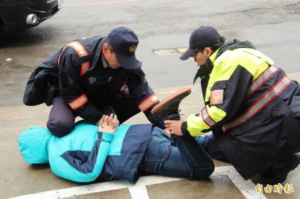 新竹縣新埔警分局偵查隊員扮演的搶匪，不顧天雨地濕，非常入戲地摔倒在地，被派出所員警們壓制後逮捕。（記者黃美珠攝）