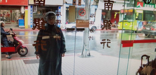 扮歹徒的警員一身深色雨衣、頭戴安全帽地走進銀行內。（記者陳恩惠翻攝）