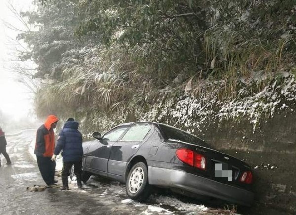 新竹縣尖石鄉鄉道竹60線後山路段因下雪導致路面結冰濕滑，就有小客車失控打滑，輪胎陷入邊溝中動彈不得。（圖由尖石鄉公所提供）