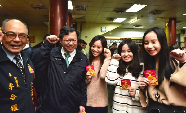 桃園市長鄭文燦（左二）發放春節福袋，與民眾比狗年手勢互動。（記者李容萍攝）