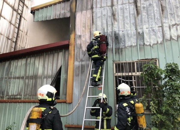 烏日今天清晨發生鐵皮廠房火警，現場不斷竄出濃煙，消防人員冒險攀爬雙節梯滅火。（記者陳建志翻攝）