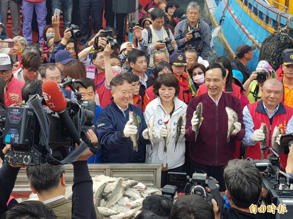 圖為漁船返港卸下滿簍的鱸魚，新北市長朱立倫（右二）議員白珮茹（右三）、民政局長江俊霆（右四）人手一尾鱸魚，祝福大家年年有餘。。（記者俞肇福攝）