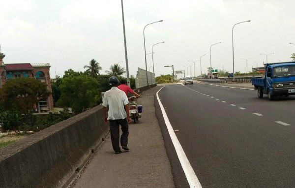 陳力仁幫阿公牽機車沿路肩走下新營交流道，阿公跟在後頭，陳中和押後戒護。（記者楊金城翻攝）