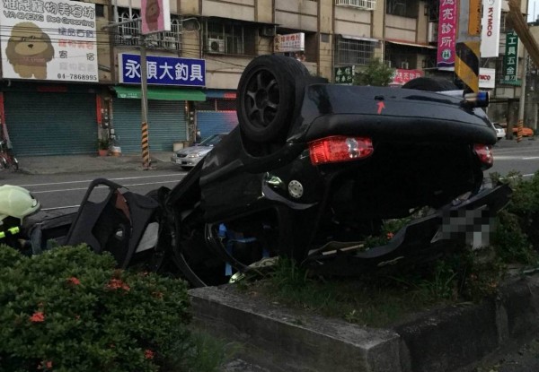 轎車撞斷路樹後翻覆在中央分隔島上，撞成廢鐵，消防員將陳姓駕駛救出送醫急救。（記者湯世名翻攝）