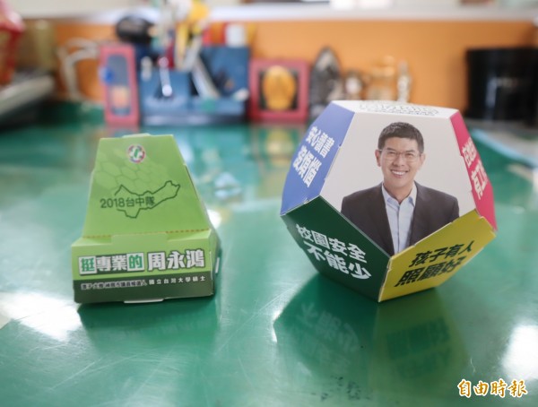 台中市第五選區市議員參選人周永鴻推出的手機架名片座及撲滿。（記者歐素美攝）