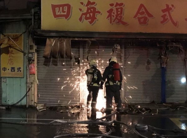 台中亞洲大學旁柳豐路的一間鐵皮屋今天凌晨起火燃燒，造成一家早餐店和2家飲料店遭波及，消防人員以電鋸破壞鐵捲門搶救。（記者陳建志翻攝）