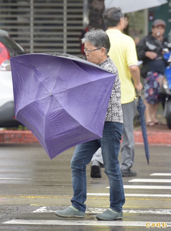 台北市區內午後仍有強風、陣雨，路上民眾緊抓雨傘前行。（記者黃耀徵攝）