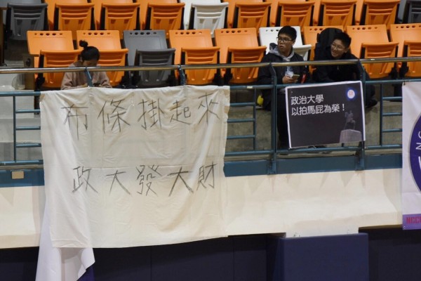 不滿的學生在校方所掛的布條前舉起了「打造政大性愛摩天輪」、「建立政大海景第一排」、「布條掛起來、政大發大財」等抗議標語。（圖擷取自「政大野火陣線」）