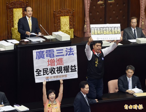 立法院新會期今天開議,朝野立委上演證所稅攻防戰,立法院長王金平召集朝野協商後宣布開會,在表決大戰中,國民黨立委張慶忠(右)跪在議事桌上呼籲速審兩岸協議監督條例,台聯立委周倪安(左下)也高舉標語高喊儘速通過廣電三法的訴求。(記者廖振輝攝)