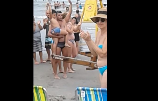 巴西一名男童在海灘走失,找不到媽媽,有個壯漢遊客把他抱起,其他遊客見狀紛紛拍手鼓掌,吸引媽媽注意,順利讓母子重逢。(圖擷取自「ViralHog」YouTube影片)