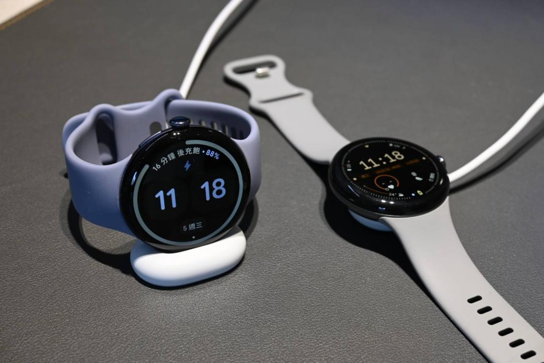 相較前代 Pixel Watch 3（右）充電是水平擺放，錶帶會佔據較多桌面空間，Pixel Watch 4（左）的充電座就能將錶帶扣起來，節省空間的設計。（圖／記者黃肇祥攝）