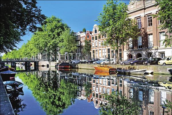 阿姆斯特丹被綠蔭籠罩的運河，倒映著美麗的山形牆建築。