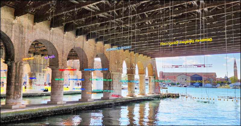 在軍火庫展區的義大利國家館外的運河旁，懸掛著各種語言翻譯的字樣，從語言中的「外語」突顯差異性。