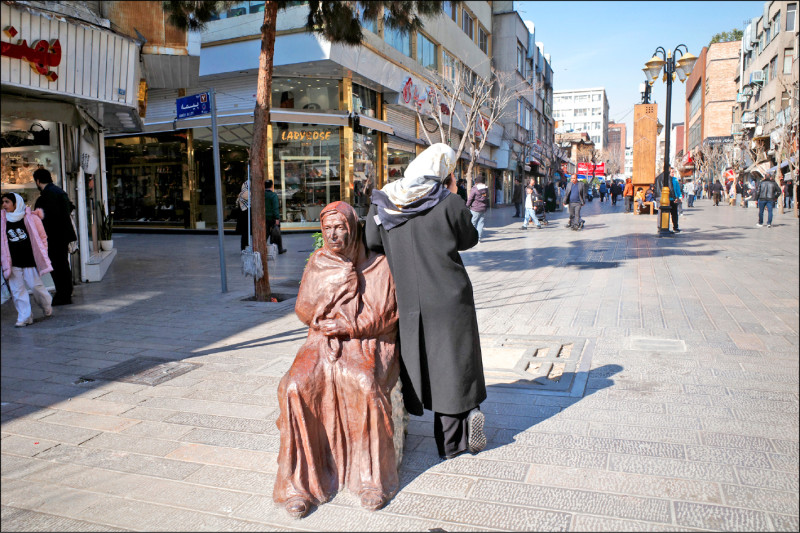 在伊朗，任何正式出現的女性形象，都必須符合伊斯蘭共和國的官方服儀規範。圖為德黑蘭街頭，一位緊拉著罩袍的女性雕像，倚在其上的，是位戴著頭巾、覆蓋秀髮的年輕女性。