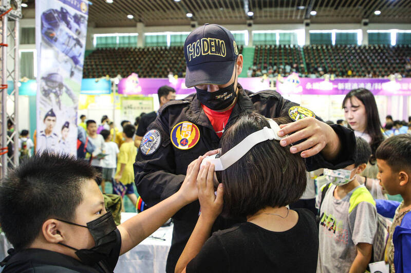 特技小組成員為小朋友配戴VR眼鏡，裡面所播放的360度特技飛行影片，可讓民眾體驗真實飛行的機內視角。（讀者黃明賢提供）