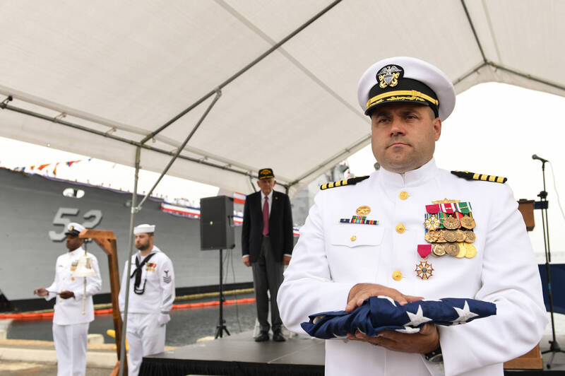神盾驅逐艦「碉堡山號」末任艦長羅傑上校（Capt. Jason Rogers）於除役典禮上手持該艦國旗，宣示該艦已完成任務，正式退役。（美軍DVIDS官網）