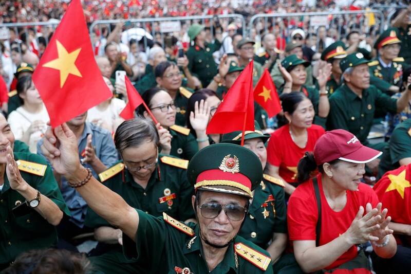 越南老兵身著軍服，在河內街頭揮舞國旗，一同觀看紀念獨立80週年的盛大閱兵。（路透）