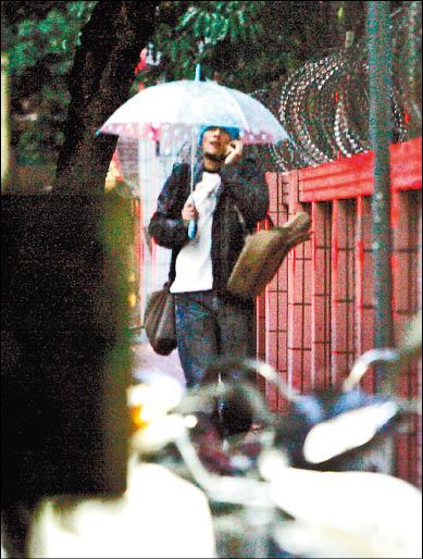 ■楊一展右肩背背包左肩掛吉他,邊撐雨傘邊撥手機。 ■楊一展右肩背背包左肩掛吉他,邊撐雨傘邊撥手機。