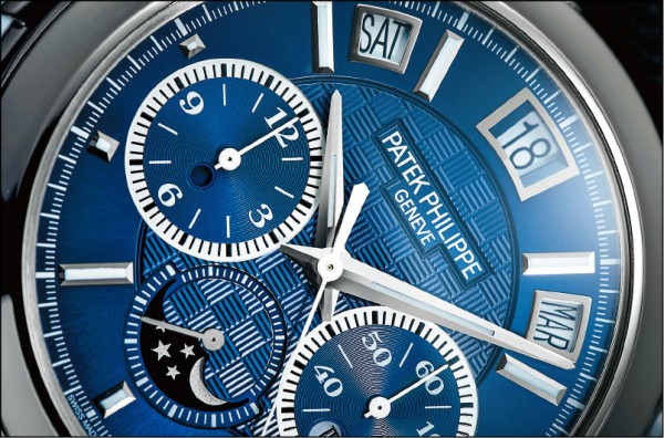 百達翡麗5208T-010腕錶的迷人布局：藍色手工雕紋錶面與夜光漆金質時標，18K白金製的日期、星期、月份顯示窗框邊皆經錘打和鑽石打磨。