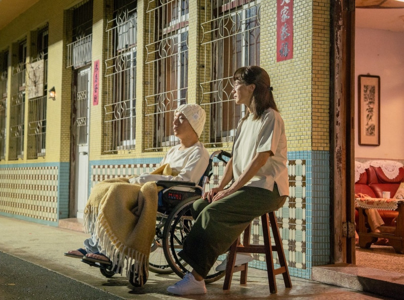 派翠克（左）在《他的靈魂與他的書店》戴著毛帽坐在輪椅上，與飾演二姊的黃采儀（右）靜靜相伴，細膩呈現血癌患者抗癌期間的溫馨片刻。