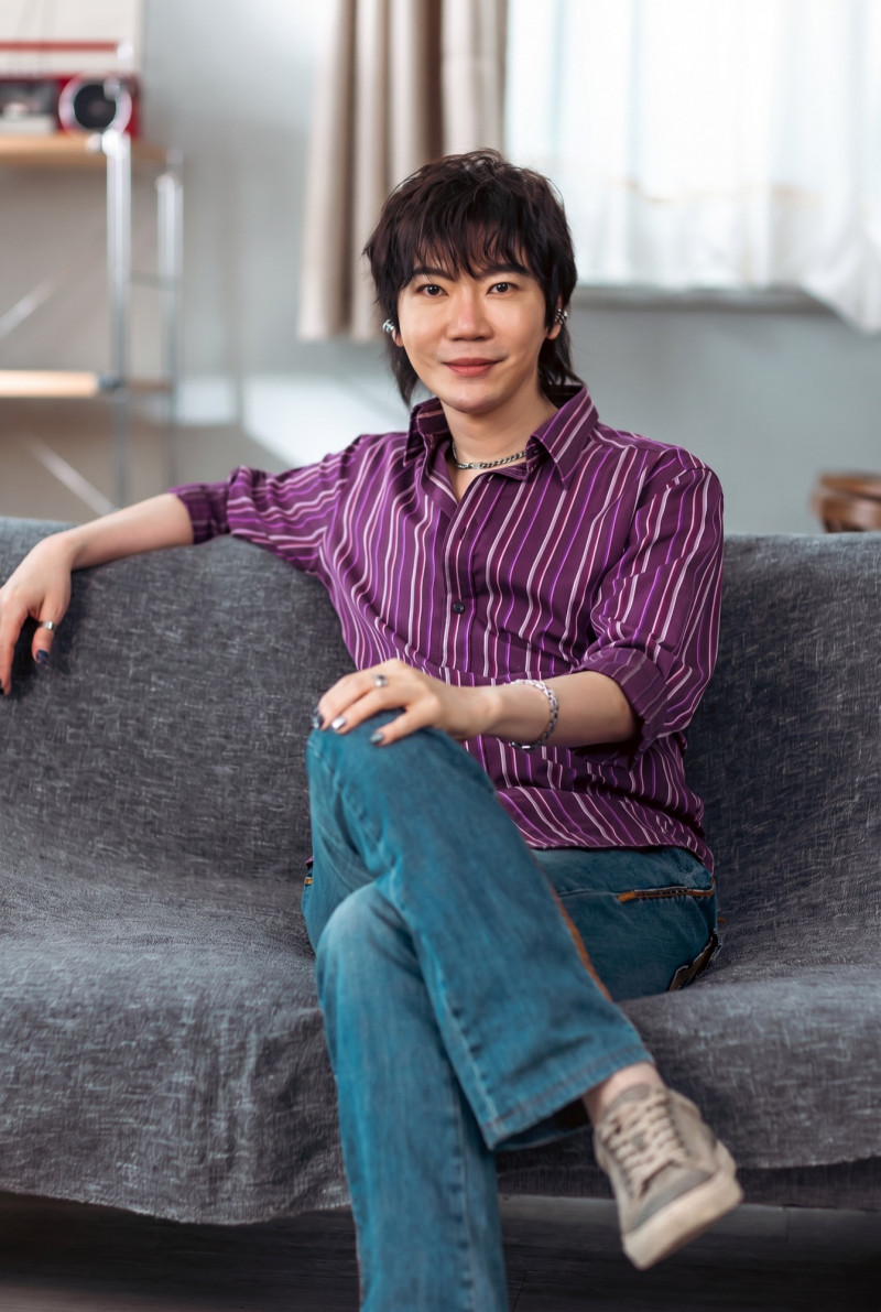 紫色のストライプシャツ姿でソファに座る歌手・達特