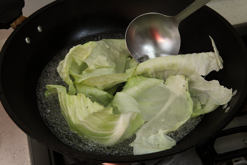 起鍋開大火，倒適量水，水滾時放高麗菜葉汆燙至熟後撈起瀝乾。
