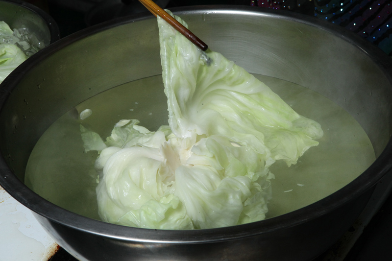 先將整顆高麗菜用尖刀去除中心的菜梗，再放入熱水中燙熟，再將熟透的高麗菜一片一片撈起，放入冷水中。