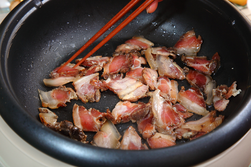 起一熱油鍋，油溫約160℃，把臘肉先爆香，約5分鐘後，觀察肉的邊緣有一點點微焦，再將蒜白部分先下鍋炒香。