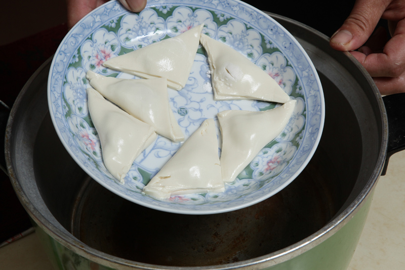 打開紗布取出豆腐餃，輕放於圓盤上，重複上述步驟繼續完成豆腐餃後，放於電鍋蒸約8分鐘。於炒菜鍋中倒入半杯水，待水煮沸後，將紅蘿蔔片、魚板片、豌豆莢一起入菜鍋，再加入1小匙鹽、1小匙太白粉調味、勾芡，淋在豆腐餃上即完成。