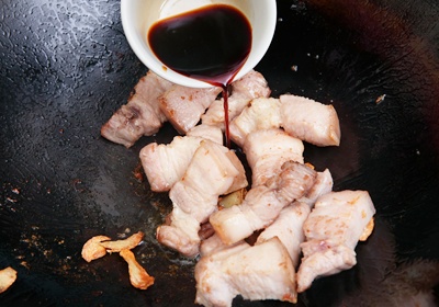 待五花肉塊焦黃後，加入醬油2匙半、白砂糖、米酒少許進行調味。