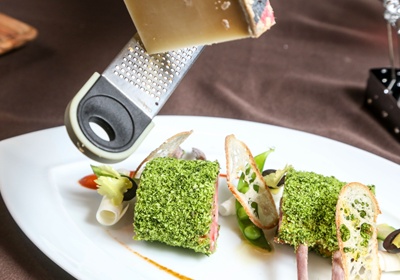 盤底以鯷魚蔬菜番茄醬點綴，先放羊排再依序擺茭白筍、綠蘆筍、橄欖、含莢豌豆與麵包脆片，最後刨上起司絲條、搭配冰過的粗條起司食用即完成。