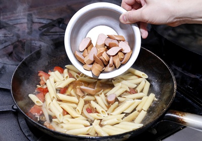 在步驟1中加入高湯，放入筆管麵與切好的Vienna Sausage片拌炒，並加入鹽與胡椒粉調味。