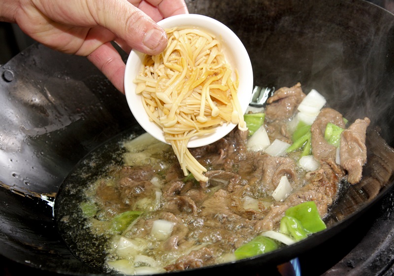 見牛肉慢慢變色，接著放入切丁的洋蔥、青椒和罐頭金針菇，泡熟後即可將油瀝乾、盛盤備用。
