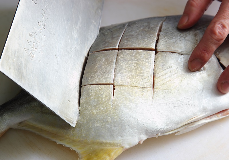 黃金鯧魚身兩面都畫上井刀痕,再泡入醃料中約15分鐘。