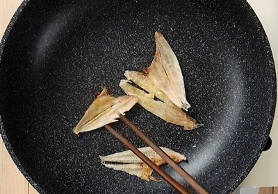 【製作湯底】熱鍋下扁魚乾煸，煸到上色後夾起剪碎備用。
