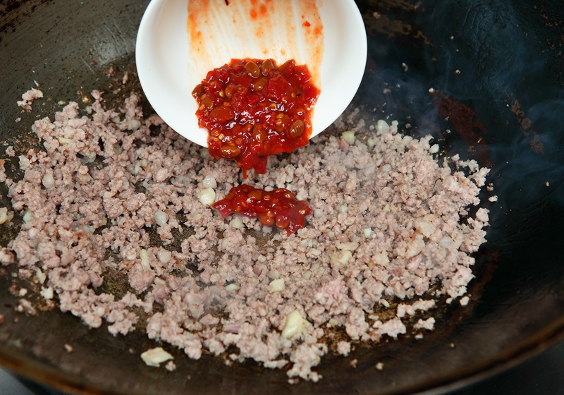 接著倒入糖、豆瓣醬拌炒約1分鐘，待豬絞肉上色。