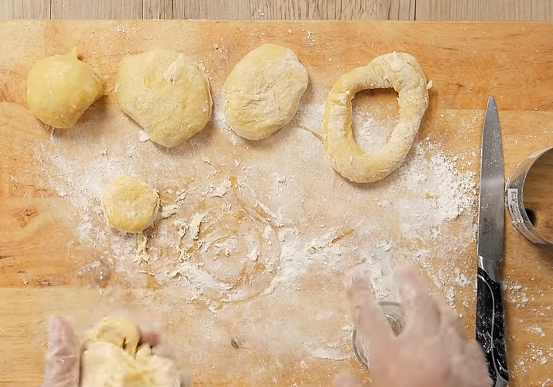 桌上灑少許手粉，將麵團分成小塊，揉成圓形，任意大小都可，用模具或杯子壓出甜甜圈中央的洞。