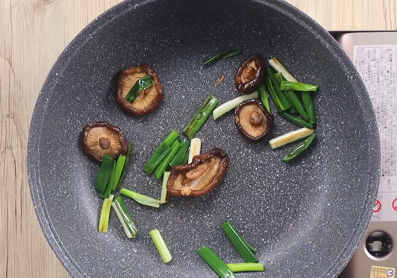 取一鍋下油、蔥段、泡發的乾香菇（擠乾，香菇水備用）炒香。