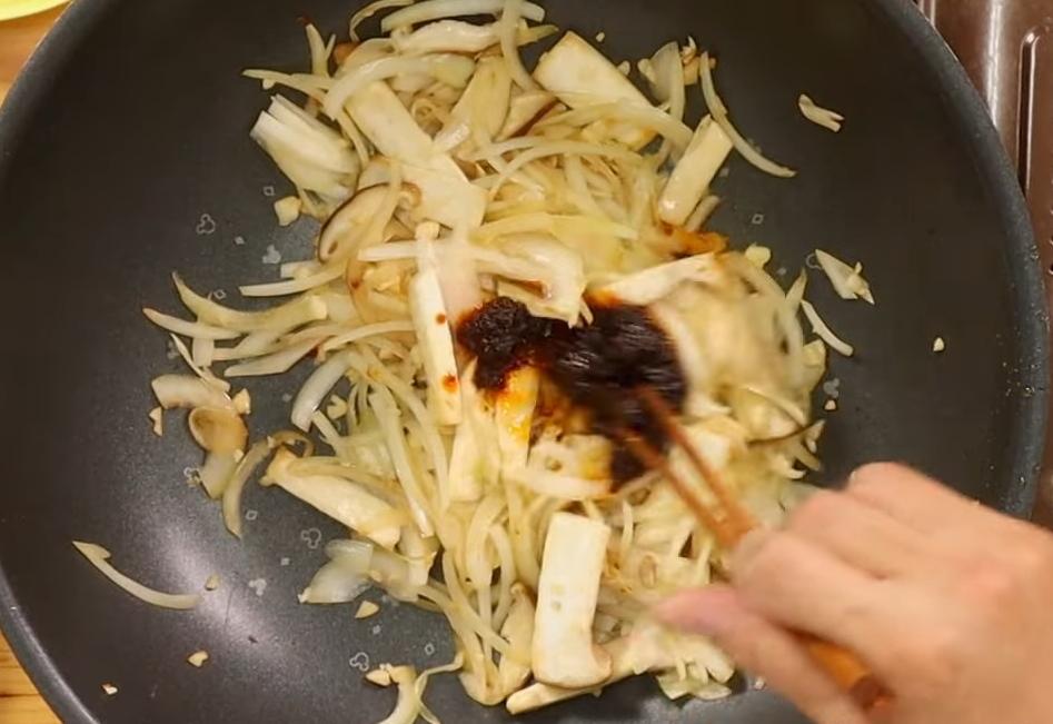 同鍋接著下洋蔥絲、蒜碎、香菇片、杏鮑菇片炒香並炒軟，再加入一些麻辣醬炒香。