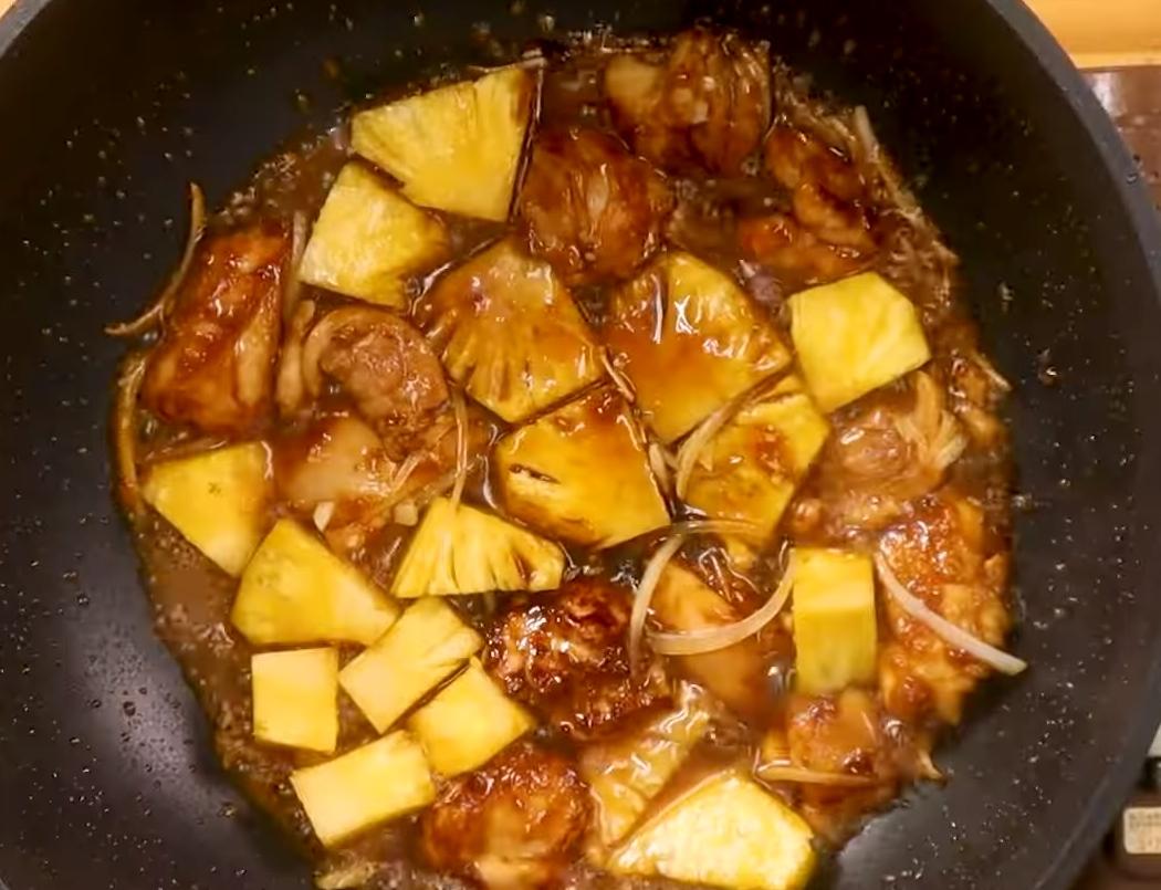 放入嫩薑、洋蔥、鳳梨跟剩餘醃料湯汁，蓋上鍋蓋小火燜煮5分鐘煨煮收汁，開蓋加適量老抽添色，放入洋蔥、辣椒拌勻裝盤，再撒上雞皮脆片、香菜跟蔥花即完成。