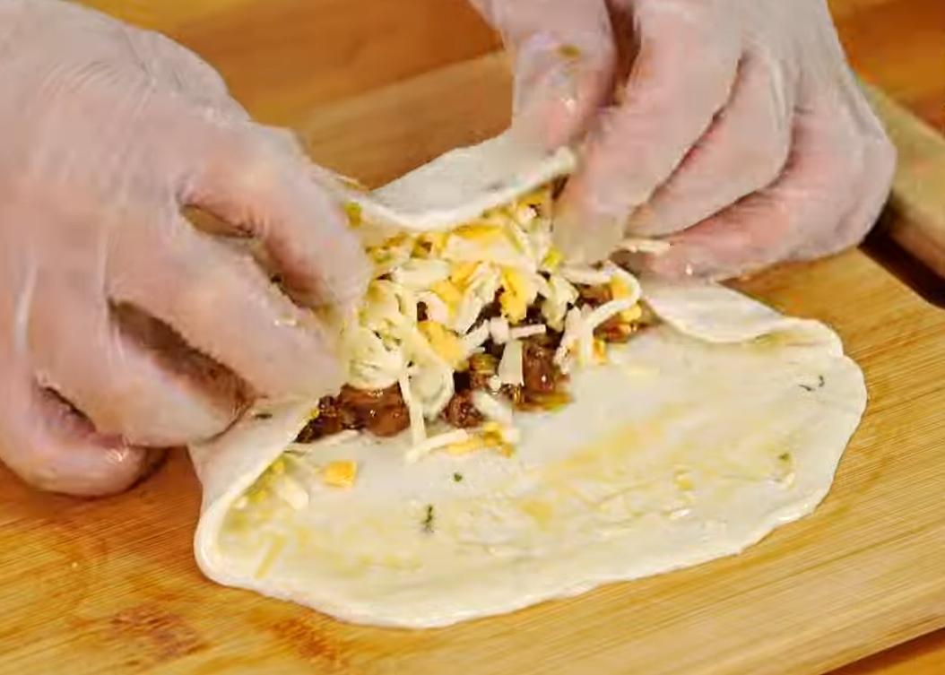 取蔥抓餅（呈半退冰狀態），鋪上肉餡及起司絲後，先將餅皮兩側向內包進再捲起。